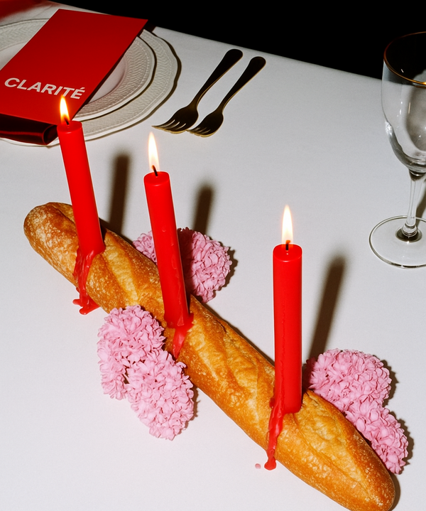 Baguette with red candles and pink flowers on a white tablecloth.