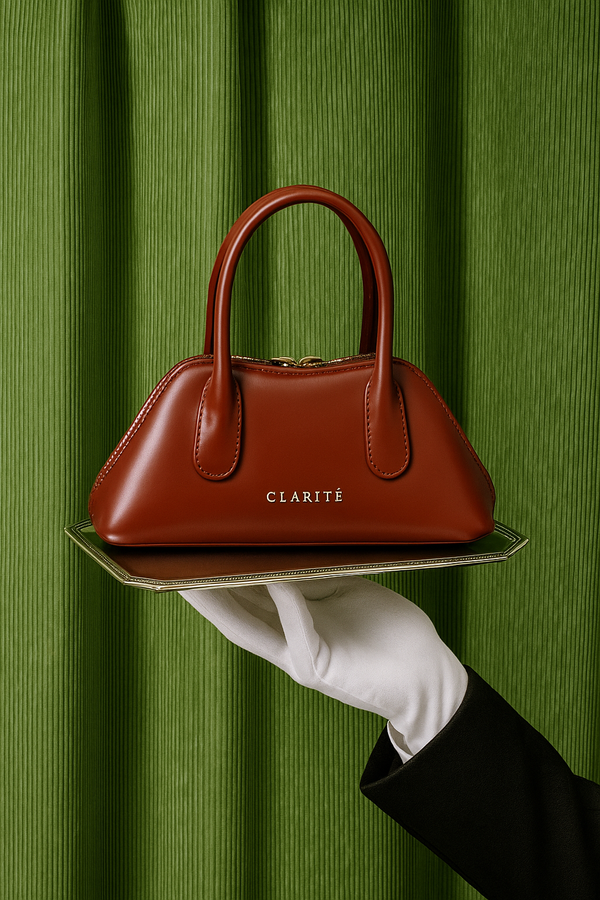 Brown handbag with 'Clarite' brand held on a tray against a green curtain background