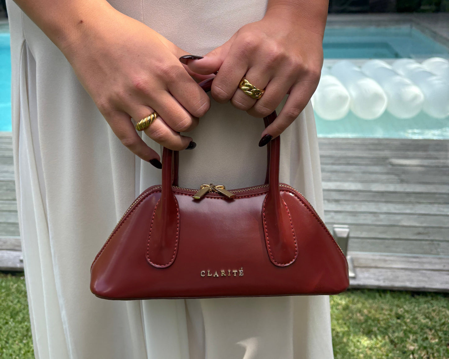 Person holding a red handbag with 'Clarite' branding against a white background.