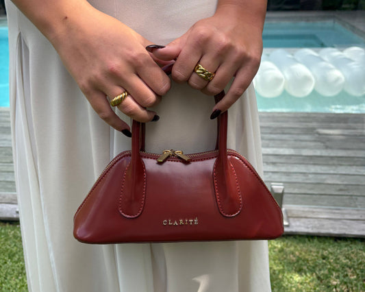 Person holding a red handbag with 'Clarite' branding against a white background.