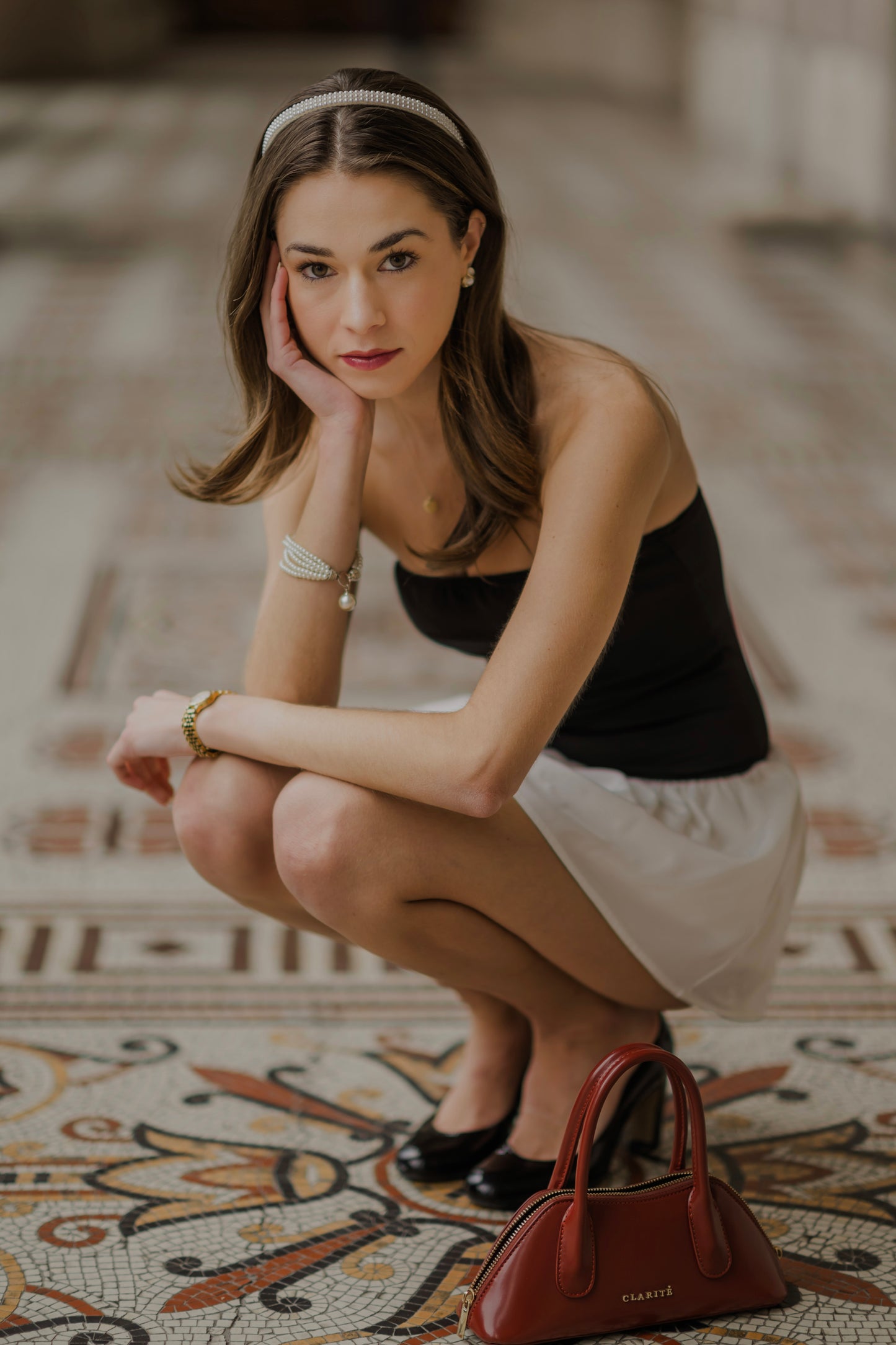 Woman squatting on a patterned floor with a handbag beside her