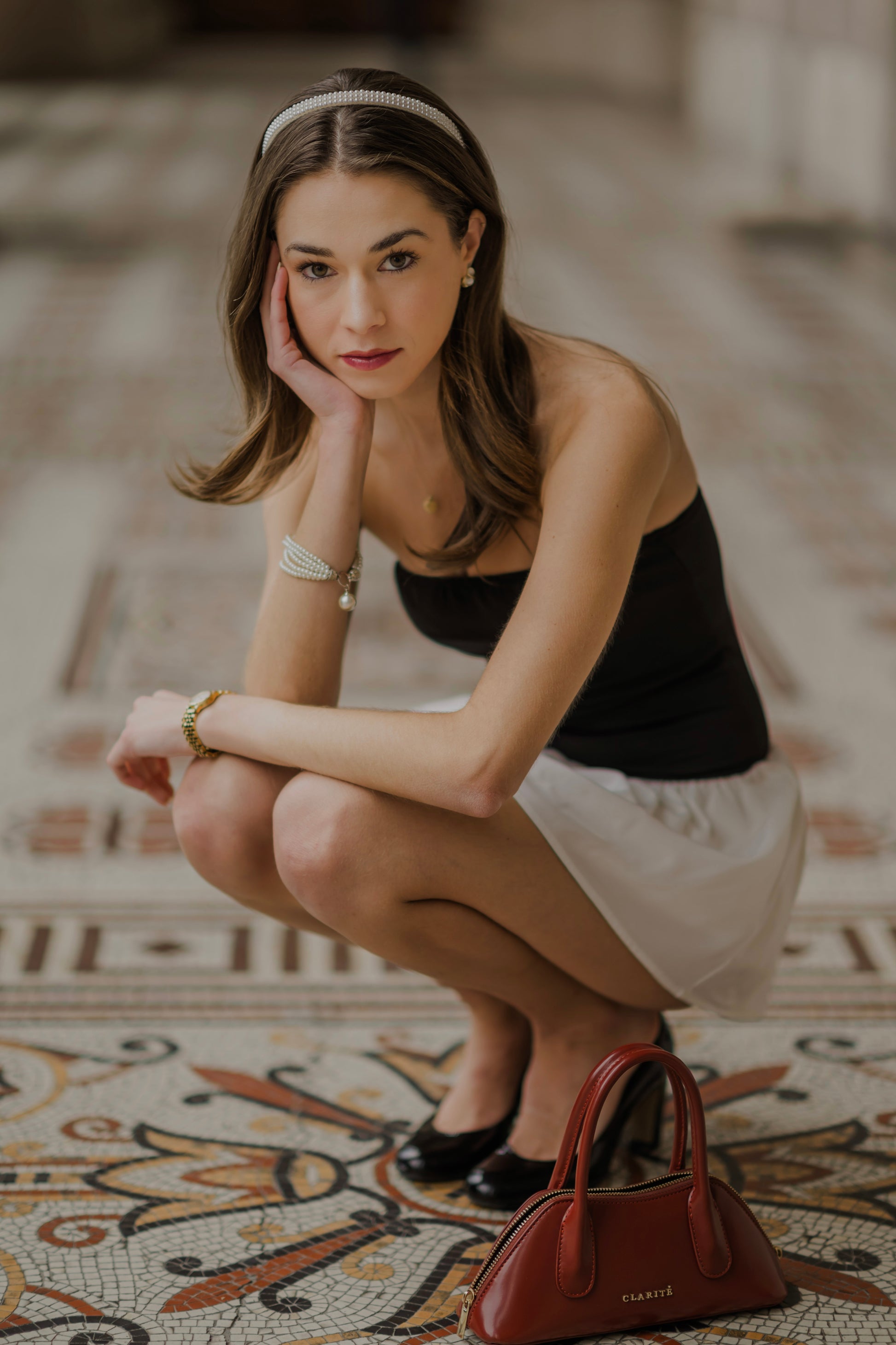 Woman squatting on a patterned floor with a handbag beside her
