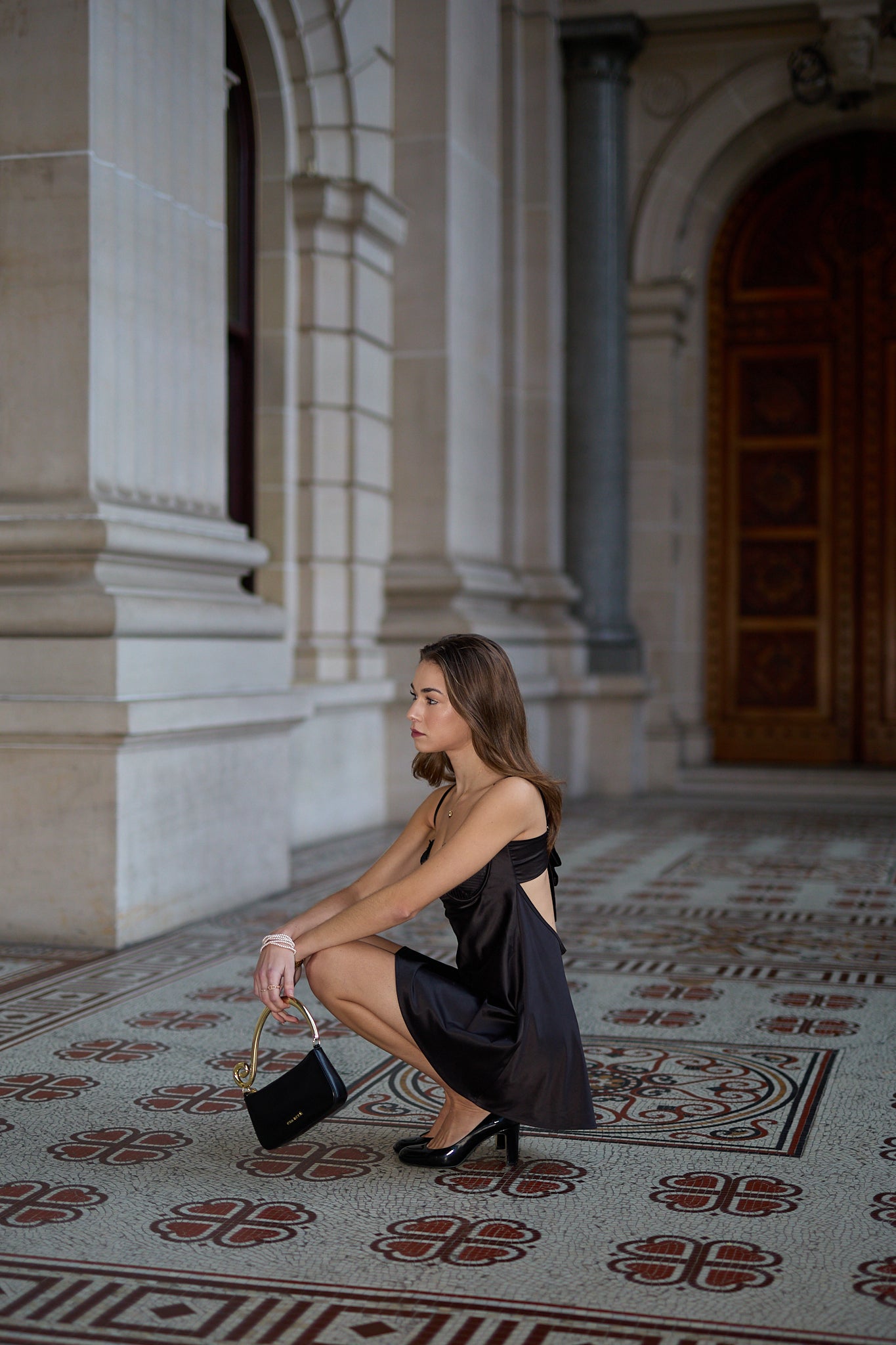 Woman in a black dress holding a handbag in an elegant interior setting