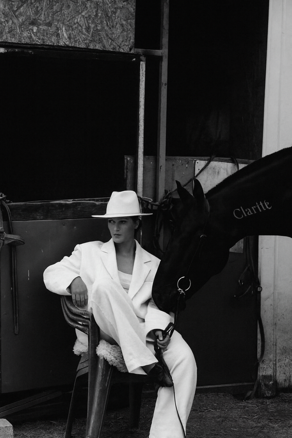 Woman in a white suit and hat sitting next to a horse with 'Clarice' on its side.