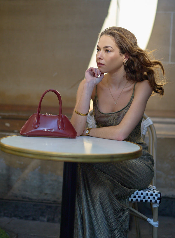 Woman sitting at a table with a red handbag in an outdoor setting