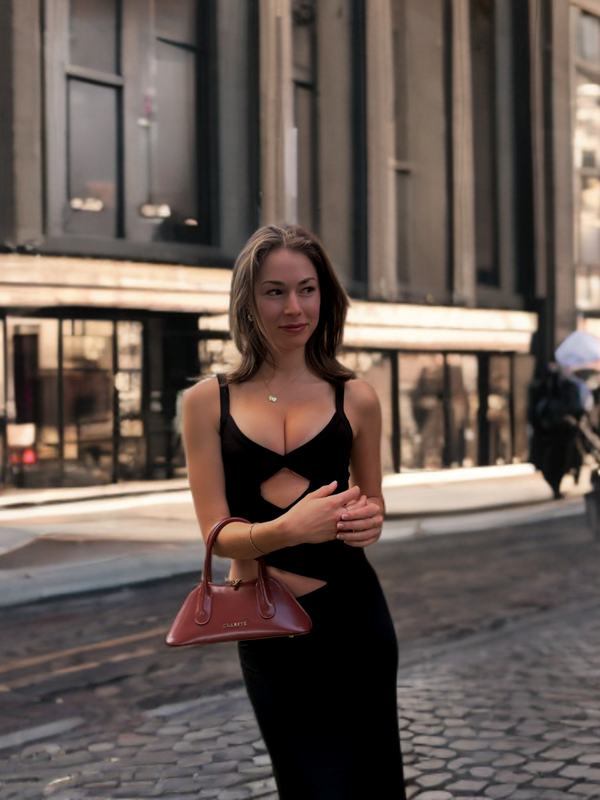 Woman in a black dress holding a red handbag on a city street.